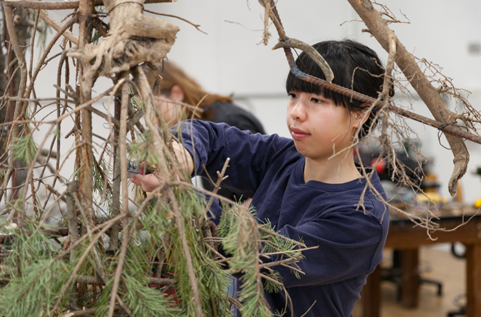 A student creates a sculpture out of natural materials for a juried outdoor exhibition.