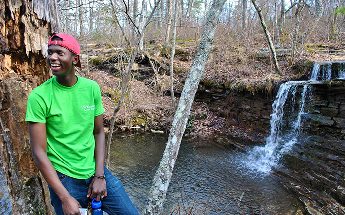 Mamadou Balde '16 smiles while leaning against a tree in front of a waterfall. Photo by Solai Sanchez '15.