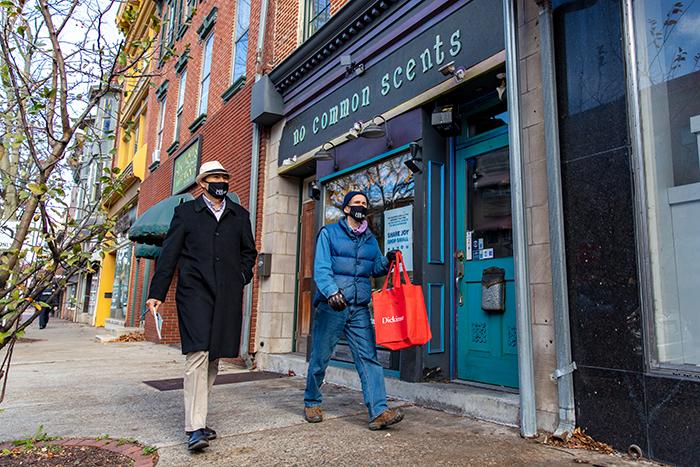 Photo of two men walking on the sidewalk in front of a store.
