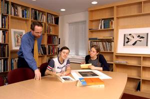 Photograph of two students and a professor reviewing a work of art