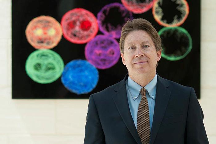 Portrait of Dale Bredesen in front of a visualization of cells.