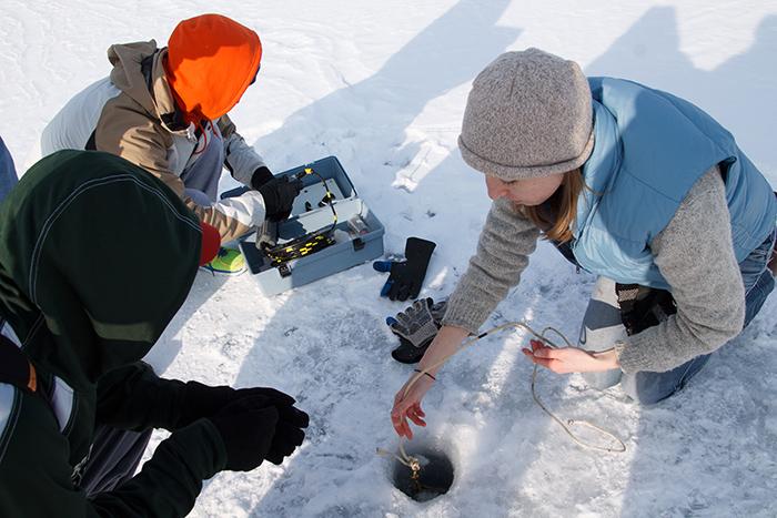Assistant Professor of Environmental Studies Kristin Strock shows students how to take lake samples through ice to determine the impact of temperature on aquatic ecosystems.