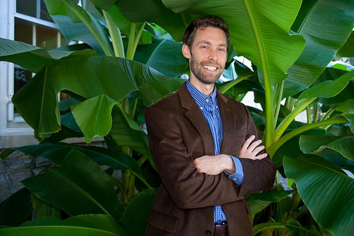 Associate Professor of Philosophy Chauncey Maher smiles under shiny, green banana leaves growing outside East College.