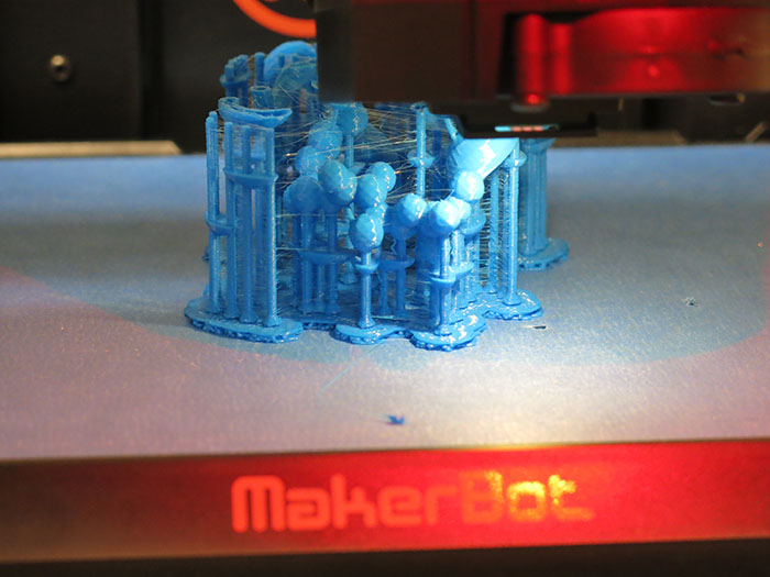 A 3D printer lays row upon row of blue plastic onto a model of a protein.