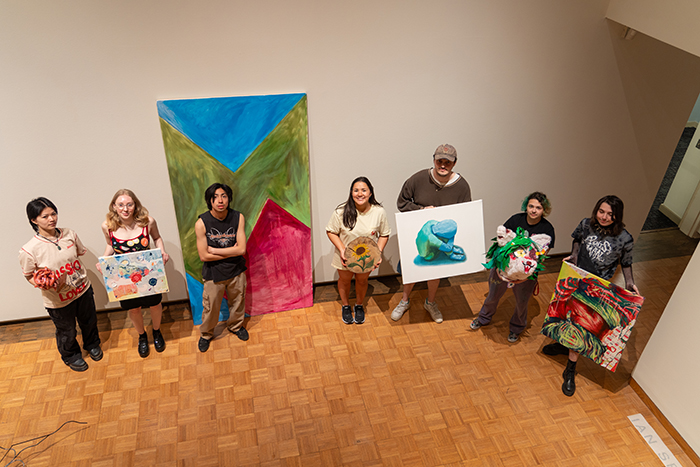 Students pose with original artworks prior to hanging their capstone joint show. Photo by Dan Loh.