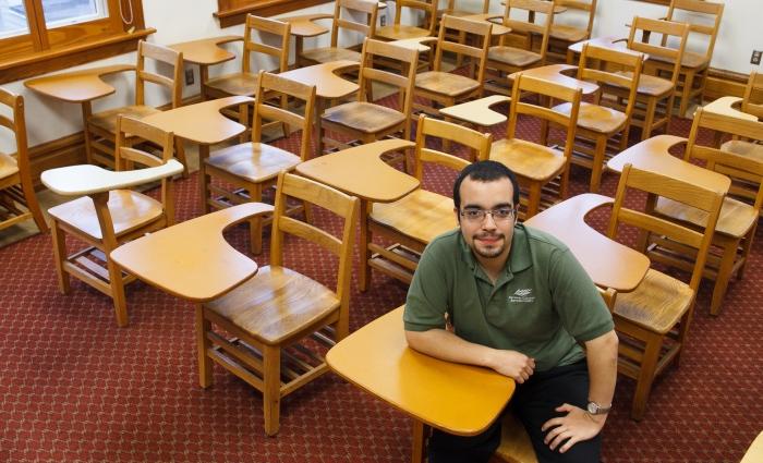 Gilbert Bonafe sits in a classroom, surrounded by desks.