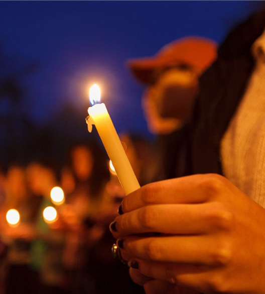 close up on a hand holding a lit candle as part of a vigil