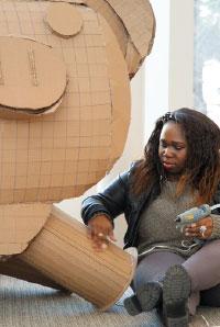 student putting finishing touches on cardboard sculpture in the library