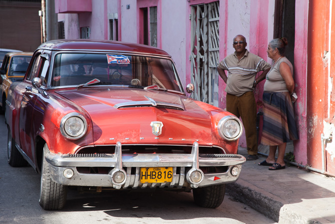 Two people standing next to a car on a Cuban street.