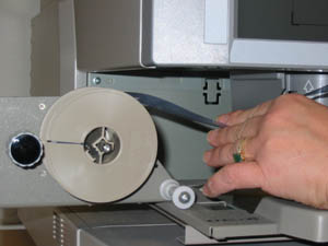 hand pulling end of microfilm from supply reel to load microfilm reader