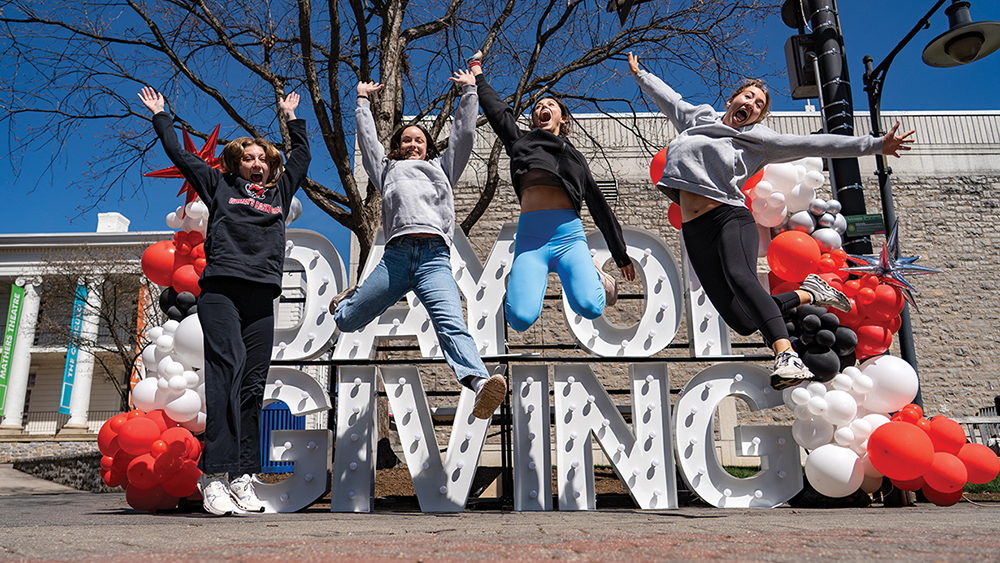 Students jumping in front of the Day of Giving sign