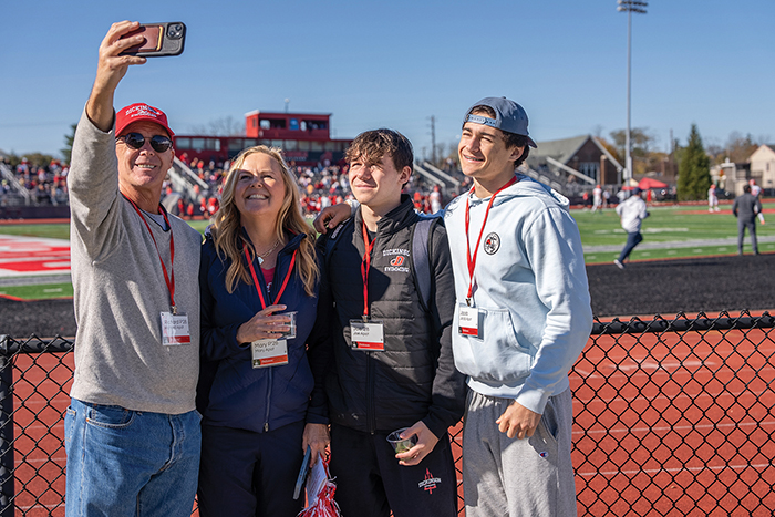 A family takes a selfie next to Biddle Field during the Homecoming and Family weekend football game