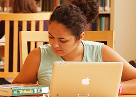 A female student sitting at a table in the library while working on her computer.