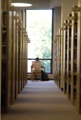 student sitting at table at far end of aisle between rows of bookshelves in the library