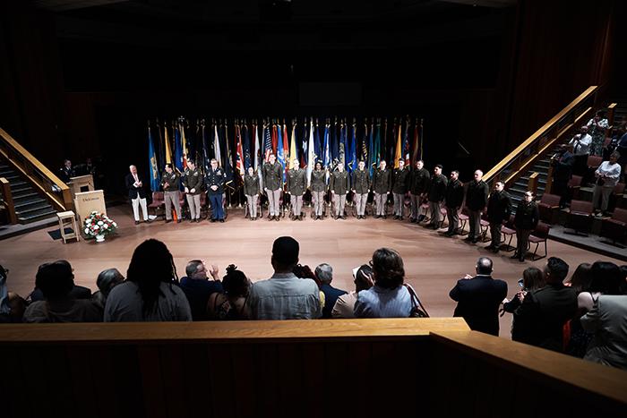 A line of soldiers standing in the center of an auditorium with a line of flags in the background.