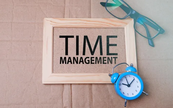 a photo of the word time management with green glasses in the top right corner and a blue analog clock in the bottom right corner