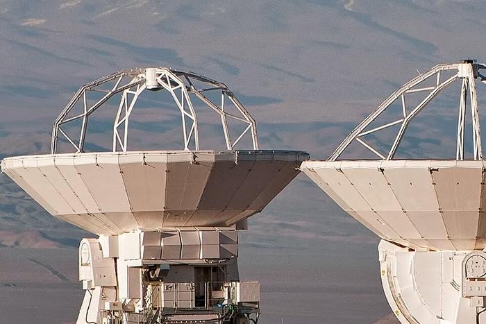 Two radio telescopes pointing toward the sky in a desert setting.