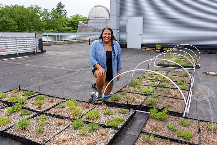 Allyssa Decker kneels behind trays of plants on the roof of Tome Hall.