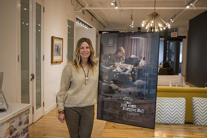 Photo of Amy Nauiokas in her office in New York City, holding a framed poster of the movie, "Can You Ever Forgive Me," which she executive produced.