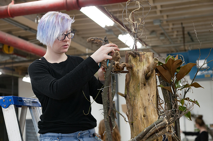 A student creates a sculpture out of natural materials for a juried outdoor exhibition.