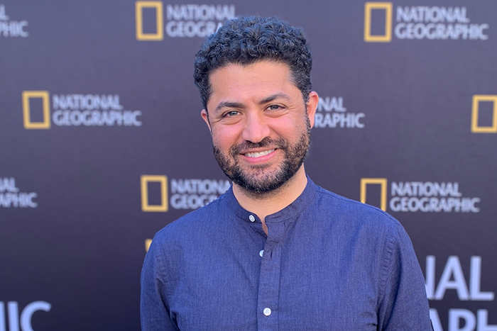 A man in a blue shirt standing in front of a banner that reads "National Geographic"