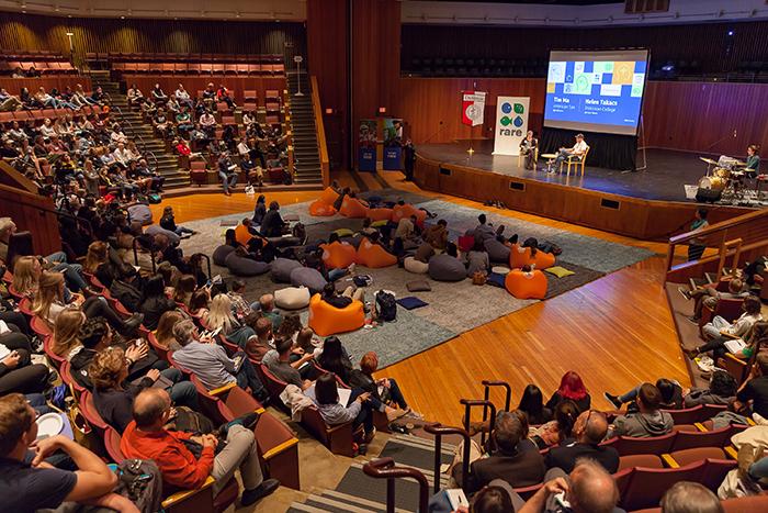 Photo of an auditorium filled with people listening to two people seated on a stage.