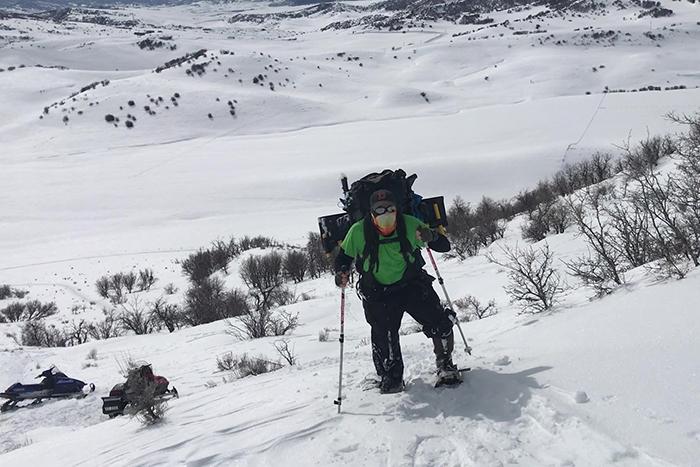 Photo of man on snowshoes walking up a steep, snow-covered hillside.