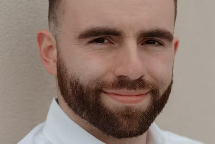 Photo of Connor Tomlinson, a bearded man standing in front of a white background.