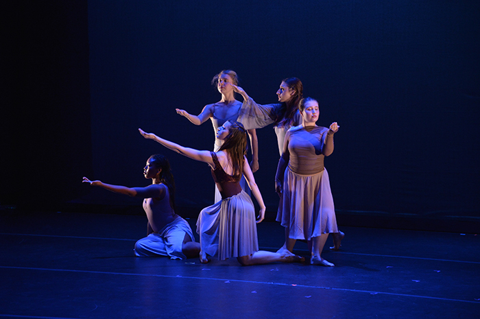 young women onstage in blue lighting, gesturing.