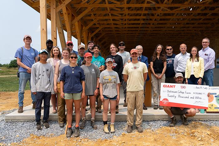 People stand at the end of a partially completed barn during a check presentation.