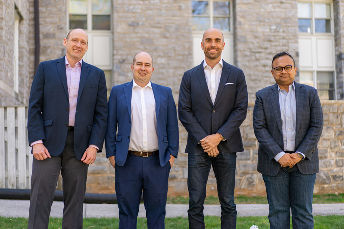 Four alums stand in front of a limestone building