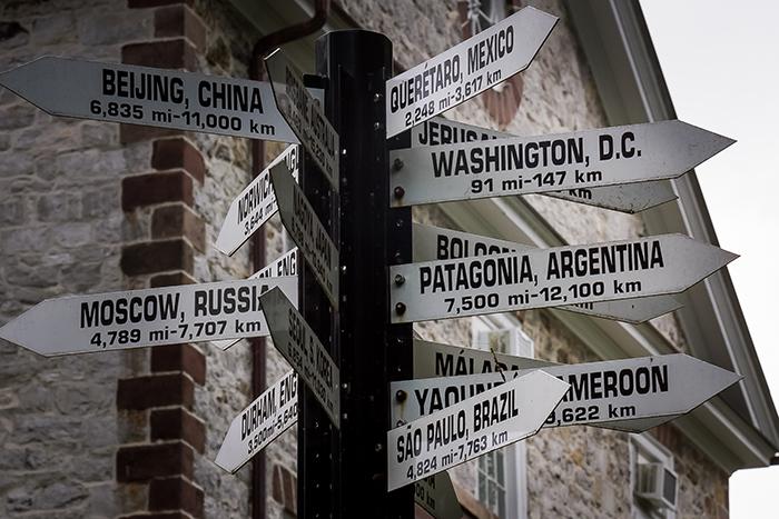 Signs pointing the direction and distance to cities around the world are displayed on top of a tall pole on Dickinson's academic quad.
