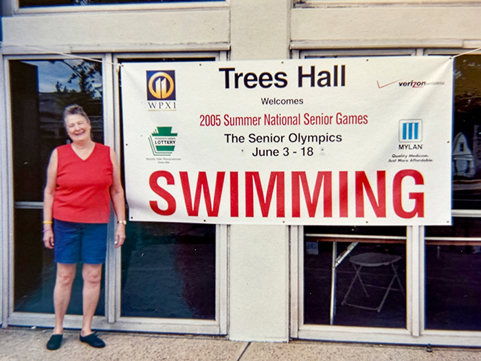 A woman poses next to a sign for the 205 National Senior Games.