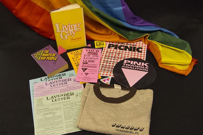 A collection of LGBTQ+ pamphlets and books displayed across a rainbow flag