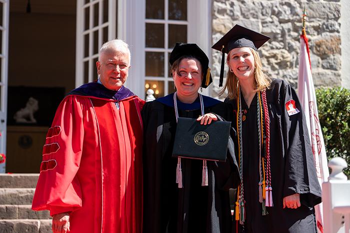 A photo of three people wearing academic robes standing in front of a limestone building.