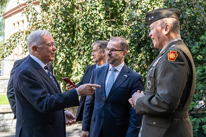 Three men greet each other in front of trees.
