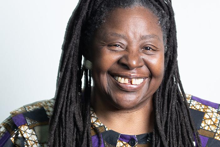 Portrait of Loretta Ross, a woman with long, black hair standing in front of a white background.