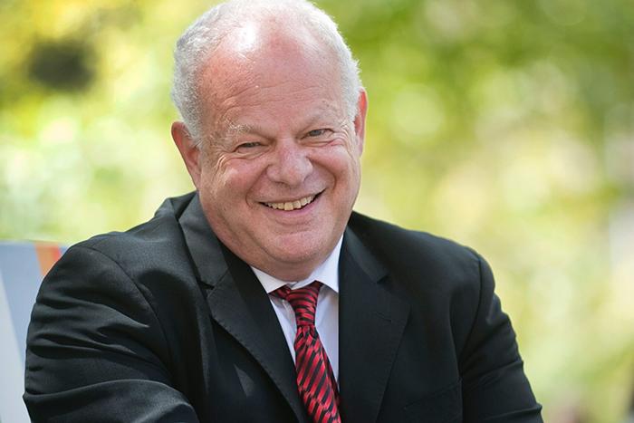 Portrait of a man in a business suit in front of a background of green trees.