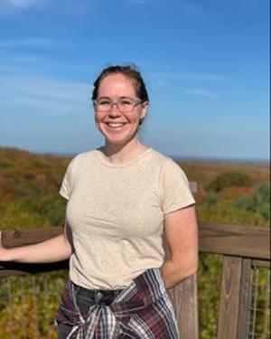 Photo of a woman standing in front of a natural scene with mountains and blue sky.