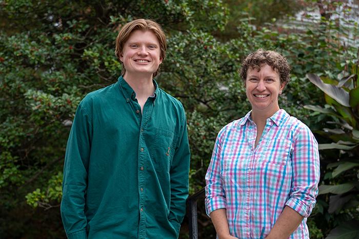 Portrait of Adam Mast and Sarah Niebler standing in front of green shrubbery.