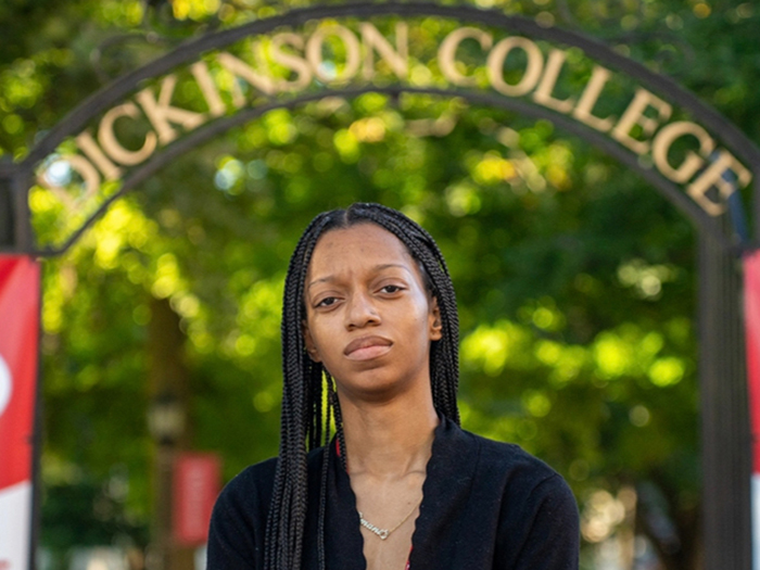 Cimani Smith '28 poses under the Dickinson College arch. She enjoys her role as a tour guide so much last spring that she opted to continue to work in that role during the summer.