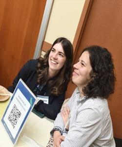 Tess, left, is sitting beside another individual at a table