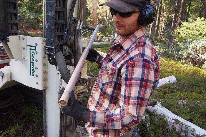 Photo of a man in a plaid shirt holding a tube containing a rock sample.