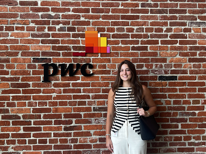 A young woman stands in front of a brick wall.