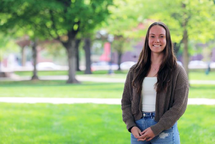 A smiling young woman stands on a green campus.