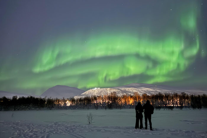 Two students look at the aurora borealis in the night sky