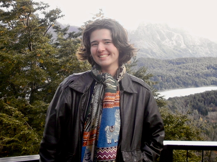 a student smiles, posing in front of a lush landscape.