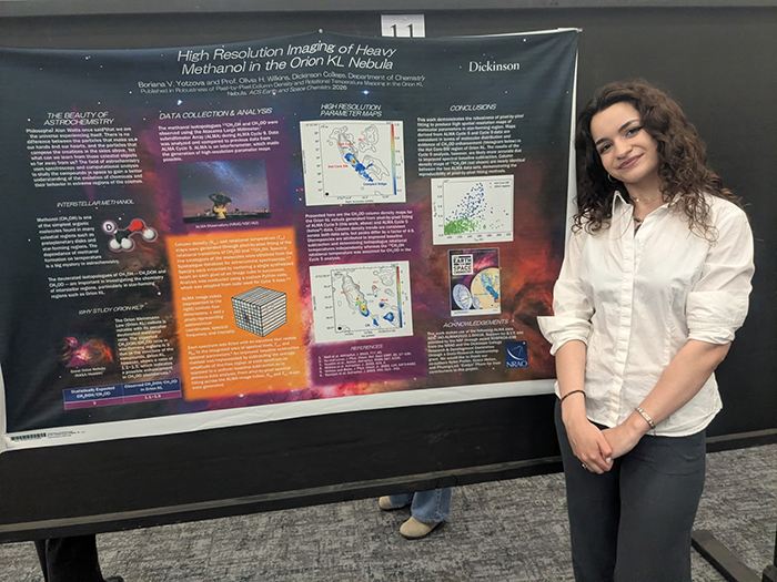A young woman stands in front of a poster displaying scientific research.