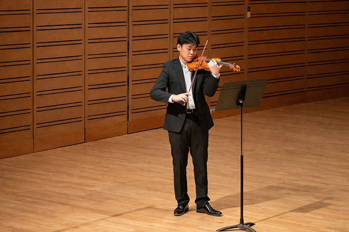 a student in a suit performs the violin onstage.