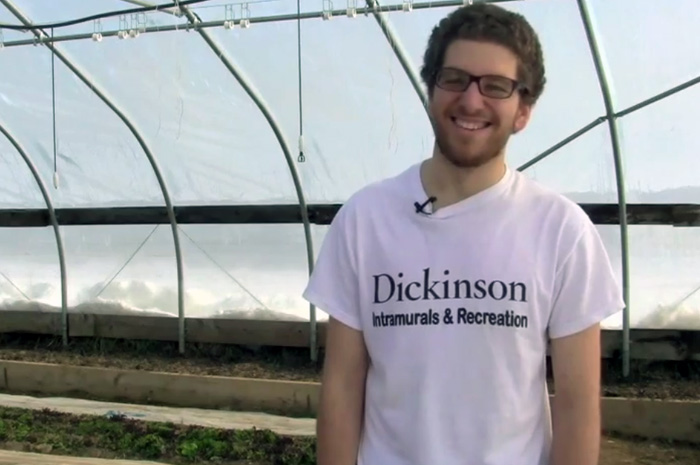 A student worker from the college farm standing in a greenhouse and smiling at the camera.